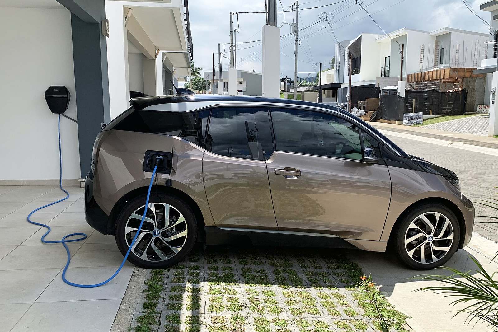 Elektrische auto op een oprit die oplaadt via een kabel aan een laadpunt tegen de muur van een woning