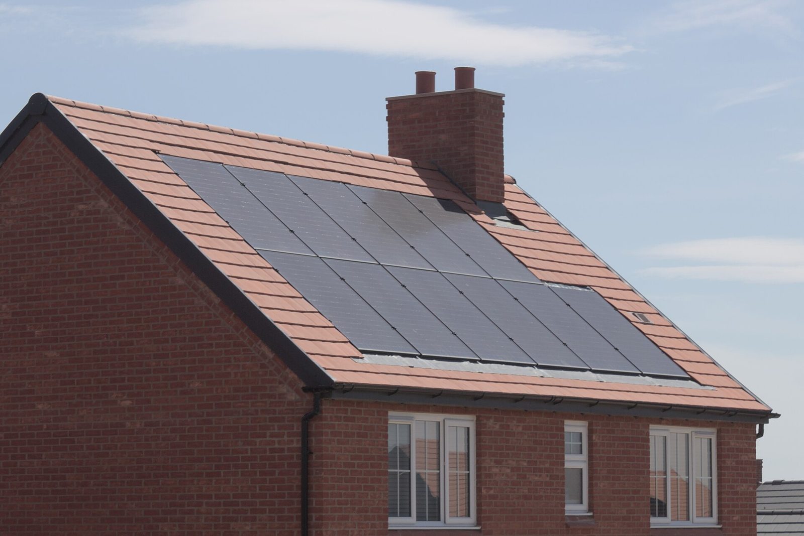 Woning in rode baksteen met een rij zwarte zonnepanelen die strak in het oranje pannendak zijn ingewerkt