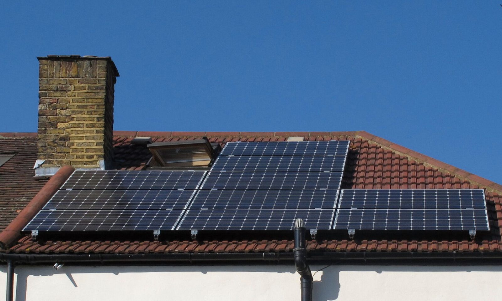 Pannendak met een rij zonnepanelen naast een bakstenen schouw onder een helderblauwe lucht